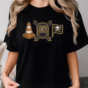 May include: Black t-shirt featuring three graphic designs: a traffic cone with "CITY OF PGH" text, a welding mask, and a pirate flag with a skull and crossed tools. The designs are in shades of yellow and orange.