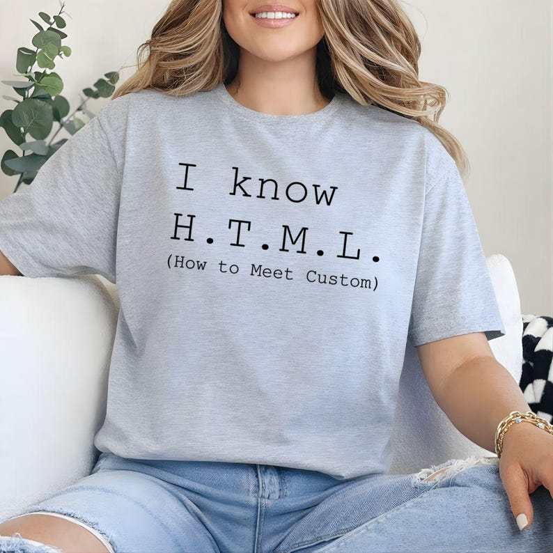 Pode incluir: Uma t-shirt de manga curta cinzenta clara com texto preto que diz I know H.T.M.L. (How to Meet Custom) impresso numa fonte estilo m&aacute;quina de escrever no peito. A pe&ccedil;a de vestu&aacute;rio tem um decote redondo e um corte padr&atilde;o.