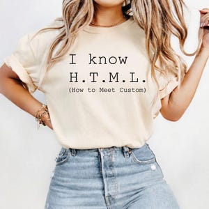 Pode incluir: Uma t-shirt de manga curta na cor creme com texto preto que diz I know H.T.M.L. (How to Meet Custom) centralizado no peito. A t-shirt tem gola redonda e &eacute; combinada com cal&ccedil;as de ganga azul claro.