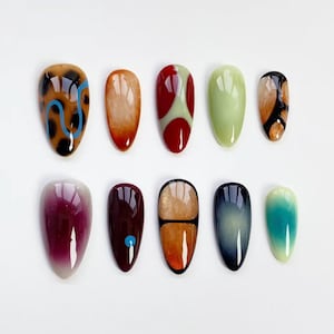 May include: Ten oval-shaped artificial nails in various designs. The nails feature colours like brown, red, green, and blue, with patterns including animal print, gradients, and geometric shapes. The nails are arranged on a white surface.