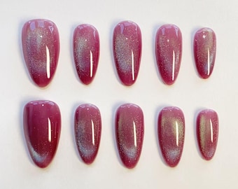 May include: A set of ten almond-shaped press-on nails in a deep magenta hue. Each nail features a reflective cat-eye magnetic finish that creates a shimmering silver streak across the center, providing a glossy and smooth surface texture.