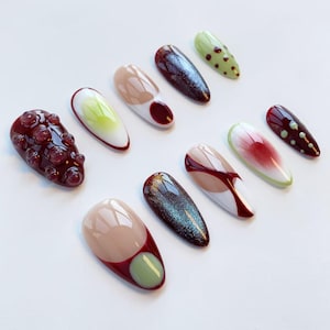 Peut inclure: Une collection de dix faux ongles aux designs vari&eacute;s. Les ongles pr&eacute;sentent des couleurs comme le bordeaux, le beige, le vert et le teal iris&eacute;. Certains ongles ont des d&eacute;tails textur&eacute;s ou &agrave; motifs, tandis que d'autres ont une finition brillante.
