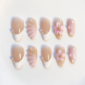 Pu&ograve; includere: Set di dieci unghie finte in vari design. Alcune unghie presentano una base nude con una punta francese bianca e dettagli di perline dorate. Altre hanno fiori rosa e abbellimenti di perle. Le unghie sono di forma ovale.