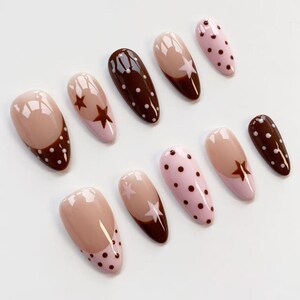 Puede incluir: Un conjunto de diez u&ntilde;as artificiales con varios dise&ntilde;os. Las u&ntilde;as presentan una combinaci&oacute;n de colores, incluyendo nude, rosa y marr&oacute;n. Algunas u&ntilde;as tienen patrones de estrellas y lunares, mientras que otras tienen un dise&ntilde;o de dos tonos.