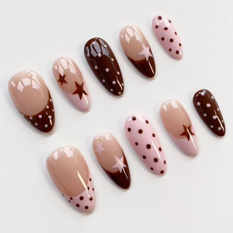 Puede incluir: Un conjunto de diez u&ntilde;as artificiales con varios dise&ntilde;os. Las u&ntilde;as presentan una combinaci&oacute;n de colores, incluyendo nude, rosa y marr&oacute;n. Algunas u&ntilde;as tienen patrones de estrellas y lunares, mientras que otras tienen un dise&ntilde;o de dos tonos.