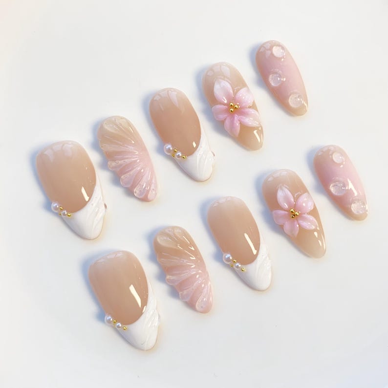 Pu&ograve; includere: Un set di dieci unghie finte con vari design. Alcune unghie presentano una french manicure bianca con dettagli dorati, mentre altre mostrano motivi floreali e a goccia rosa. Le unghie hanno una finitura lucida.