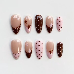 Puede incluir: Un conjunto de diez u&ntilde;as postizas ovaladas. Las u&ntilde;as presentan una variedad de dise&ntilde;os, incluyendo colores lisos, lunares y detalles de estrellas. Los colores incluyen marr&oacute;n, rosa y nude.