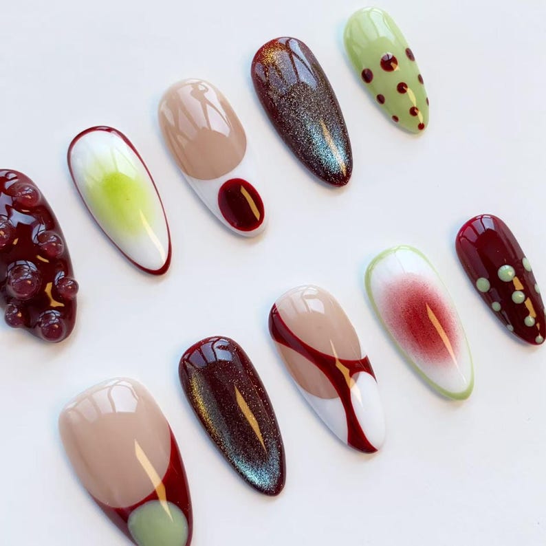 Peut inclure: Une collection d'ongles artificiels peints avec divers motifs. Les ongles pr&eacute;sentent des couleurs comme le rouge, le vert, le beige et le blanc, avec des motifs comprenant des points, des d&eacute;grad&eacute;s et des formes abstraites. Certains ongles ont un aspect textur&eacute; en forme de bulles.