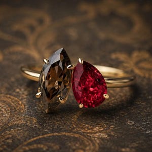 Op de afbeelding: Een gouden ring met twee opvallende edelstenen: een bruine rookkwarts in marquise-slijpvorm en een levendige rode robijn in peervorm. De stenen zijn naast elkaar gezet op een dunne, gepolijste gouden band, wat zorgt voor een contrast in vorm.