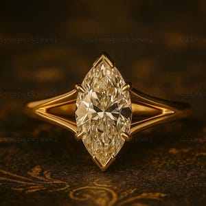 Op de afbeelding: Een marquise-geslepen diamanten ring met een gouden band. De diamant is het middelpunt, gezet in een klauwzetting. De ring wordt gepresenteerd op een donkere, patroonachtige ondergrond.