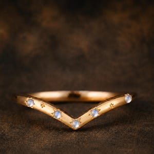 May include: A gold V-shaped ring featuring four small, round, iridescent moonstones set into the band. The metal band is accented with engraved star motifs between the stones, creating a celestial-inspired design with a polished finish.