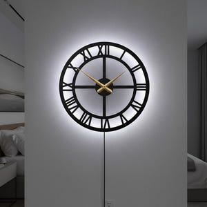 May include: A black, round wall clock with Roman numerals and gold-colored hands. The clock is illuminated with a soft white light, creating a halo effect. The clock is powered by a black cord.