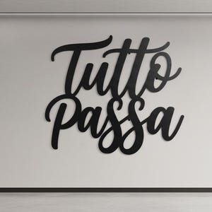 May include: Black metal wall art in a modern garage setting. The cursive text "Tutto Passa" is displayed on a white wall. The garage includes tools, shelves, and a covered car.