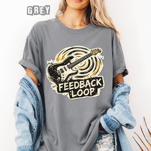 May include: Grey t-shirt with a distressed graphic of a black and gold electric guitar and the words "FEEDBACK LOOP" in a black and white rectangular design. The word "GREY" is printed at the top of the shirt.