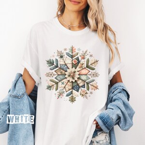 Peut inclure: T-shirt blanc avec un motif de flocon de neige coloré. Le flocon de neige est composé de formes géométriques bleues, vertes et beiges, avec des accents floraux. Le mot "WHITE" est imprimé sur l'image.