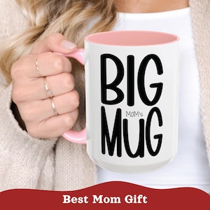 Op de afbeelding: Een witte keramische mok met een lichtroze binnenkant en handvat. De voorkant van de mok is voorzien van de zwarte tekst BIG MOM'S MUG in een vet, gestileerd lettertype. Het ontwerp is strak en eenvoudig, wat het contrast tussen wit en roze benadrukt.
