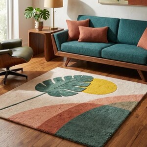 Könnte beinhalten: Ein rechteckiger Teppich mit einem botanischen Design. Er zeigt ein großes grünes Blatt, einen gelben Kreis und geschichtete Bänder in Pfirsich und Grün auf cremefarbenem Hintergrund. Der Teppich liegt auf einem Holzboden.