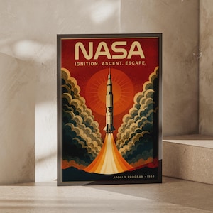 以下が含まれることがあります： NASAのロケット打ち上げグラフィックが描かれた額入りポスター。NASA IGNITION. ASCENT. ESCAPE. および APOLLO PROGRAM 1969という文字が記されている。大きなオレンジ色の太陽を背景に上昇するロケットと、周囲の暗い雲や排気ガスが描かれている。