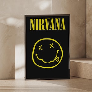 May include: A rectangular framed poster featuring a black background with the word NIRVANA printed in yellow at the top. Below the text is a yellow hand-drawn style smiley face graphic with X-shaped eyes and a tongue sticking out to the side.