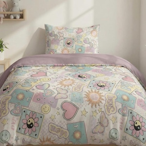 May include: A bed set with a duvet cover and pillowcase, patterned with pastel hearts, flowers, butterflies, suns, and smiley faces on a cream background. The duvet cover has a solid mauve top.