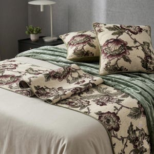 May include: A bed set featuring a floral pattern in cream, burgundy, and green. The set includes two square pillows and a long runner, all with a detailed botanical design. The bed is covered with a sage green blanket.