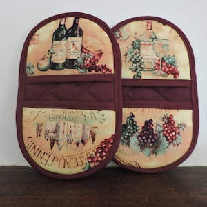 May include: A pair of red and beige oven mitts with a quilted design. The mitts feature a wine and grape motif with the text "Chateau d'Ennis Cabernet Sauvignon".