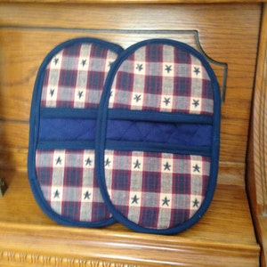 May include: Two red, white, and blue oven mitts with a navy blue trim and a navy blue pocket on the back. The mitts are made of a checkered fabric with white stars.