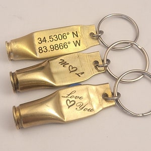 May include: Three gold bullet casing keychains with different engravings. The top keychain has the coordinates 34.5306° N 83.9866° W. The middle keychain has the initials "M & L" with a heart symbol. The bottom keychain has the words "Love You" with a heart symbol.