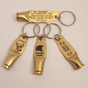 May include: Three gold-colored keychains with different designs. The first keychain features the 2nd Amendment text, the second keychain has a Spartan helmet with the text "MOLON LABE", and the third keychain has a deer silhouette and coordinates.