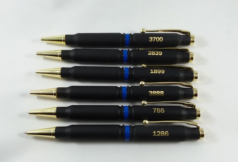 This picture is six thin Blue line police pens made out of 308 bullets it is two shells set back to back separated by a thin blue band it is a twist pen with gold components and gold accent engraving