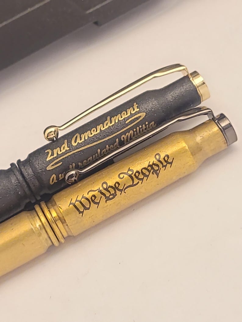 以下が含まれることがあります： 刻まれた文字が書かれた金と黒のペン2本。 上のペンには「2nd Amendment A well regulated Militia」という文字が刻まれ、下のペンには「We the People」という文字が刻まれています。