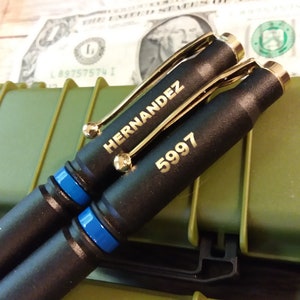 This is a picture of two thin Blue line police pens that are made out of 308 bullets. The two shells are powder coated black with a thin Blue line separator the components and engraving are both gold creating a nice offset from the flat black finish