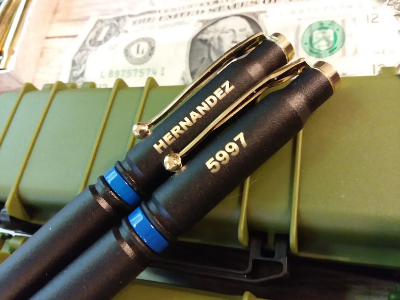 This is a picture of two thin Blue line police pens that are made out of 308 bullets. The two shells are powder coated black with a thin Blue line separator the components and engraving are both gold creating a nice offset from the flat black finish