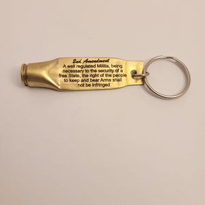 K&ouml;nnte beinhalten: Ein goldfarbener Schl&uuml;sselanh&auml;nger in Form einer Patronenh&uuml;lse mit dem Text "2nd Amendment" und dem Text "A well regulated Militia, being necessary to the security of a free State, the right of the people to keep and bear Arms shall not be infringed" eingraviert.