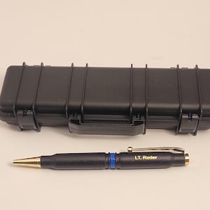 May include: A black pen with a gold tip and a blue stripe. The pen is engraved with the text "LT. Ruder". The pen is in a black hard case.