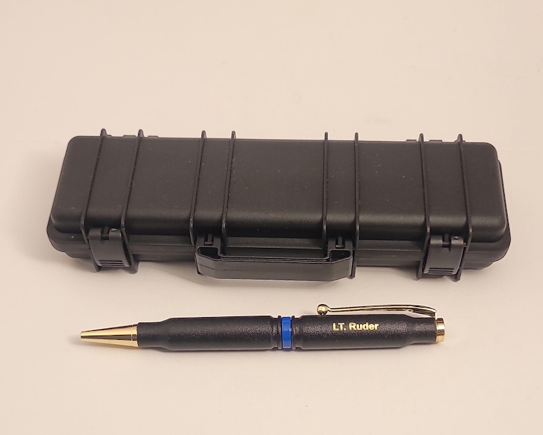 May include: A black pen with a gold tip and a blue stripe. The pen is engraved with the text "LT. Ruder". The pen is in a black hard case.
