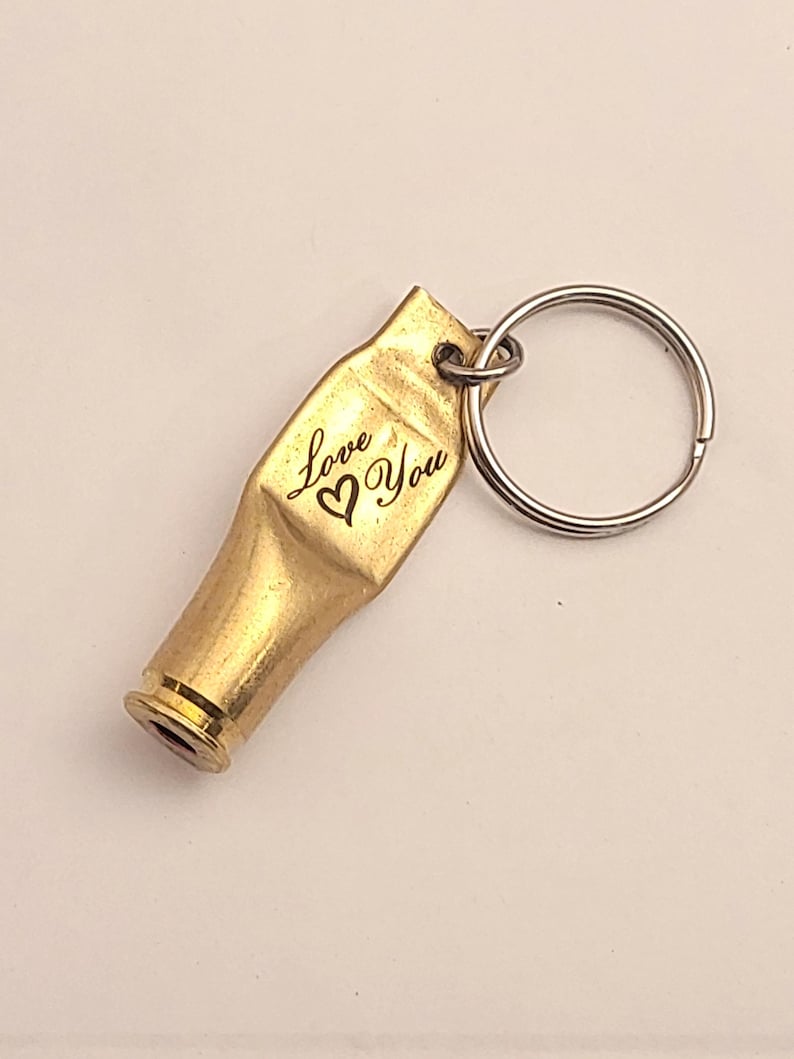 K&ouml;nnte beinhalten: Goldfarbener Schl&uuml;sselanh&auml;nger mit einem Anh&auml;nger aus einer Patronenh&uuml;lse, auf dem "Love You" und ein Herzsymbol eingraviert sind. Der Schl&uuml;sselanh&auml;nger hat einen silbernen geteilten Ring.
