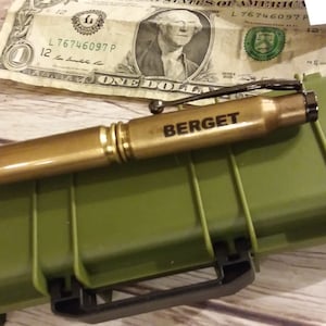 May include: A gold-colored bullet pen with a black clip and a black tip. The pen is engraved with the name "BERGET".