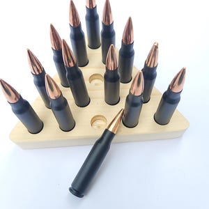 May include: A wooden triangle-shaped display stand with 18 black and copper-colored bullet casings. The casings are arranged in a triangular pattern. One casing is lying on the stand.