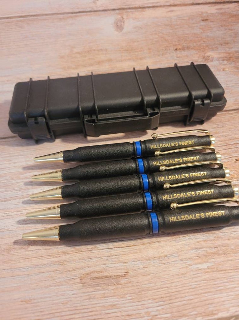 May include: Six black pens with gold accents and blue trim. Each pen has the words "HILLSDALE'S FINEST" engraved in gold lettering. The pens are in a black hard case.