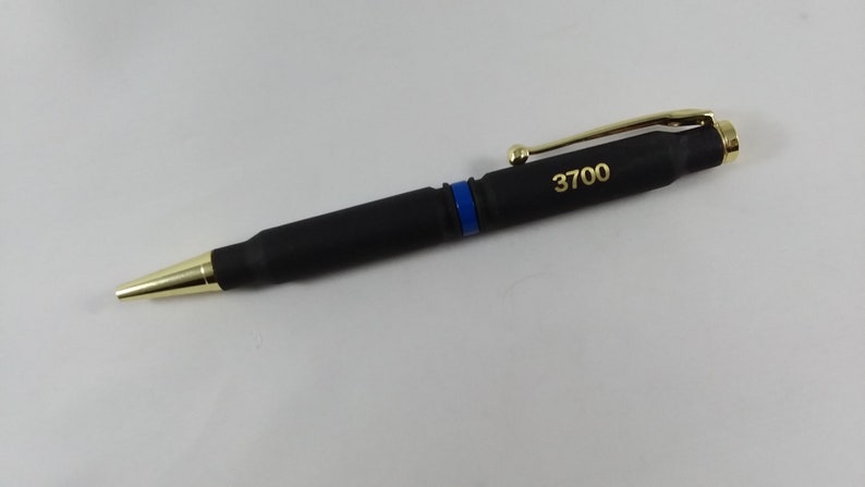 May include: A black pen with a gold clip and tip. The pen is shaped like a bullet and has a blue stripe. The number 3700 is engraved on the pen.