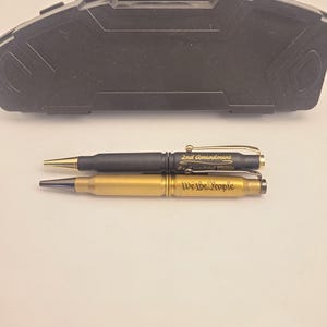 以下が含まれることがあります： 2つの弾丸ペンセット、1つは黒、もう1つは金で、テキストが刻印されています。黒いペンには「2nd Amendment」が刻印されており、金のペンには「We the People」が刻印されています。ペンは黒いハードケースに入っています。