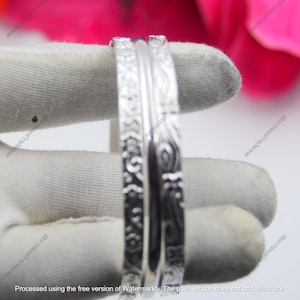 May include: Close-up of two silver bangles with detailed engraved patterns. The bangles are shown against a neutral background, emphasising their intricate designs. The jewellery is likely for fashion or personal adornment.