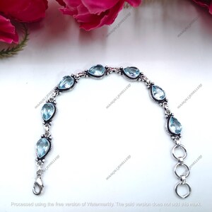 May include: A silver bracelet featuring pear-shaped, light blue gemstones. The bracelet has a delicate design with a lobster clasp closure and three connecting rings. The gemstones are set in a decorative silver setting.