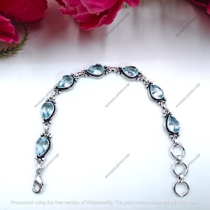 May include: A silver bracelet featuring pear-shaped, light blue gemstones. The bracelet has a delicate design with a lobster clasp closure and three connecting rings. The gemstones are set in a decorative silver setting.
