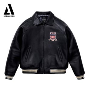 May include: Black leather jacket with a zip-up front, a collar, and a patch on the chest. The jacket has white and beige striped details on the cuffs and hem. The patch features a red, white, and blue design.