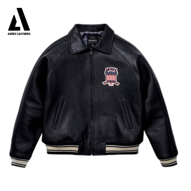 May include: Black leather jacket with a zip-up front, a collar, and a patch on the chest. The jacket has white and beige striped details on the cuffs and hem. The patch features a red, white, and blue design.
