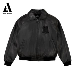 Puede incluir: Chaqueta bomber de cuero negro con cremallera, cuello y pu&ntilde;os y dobladillo de canal&eacute; negros. Cuenta con un emblema negro en el pecho y el logotipo "AUREV LEATHERS" en la esquina superior izquierda.