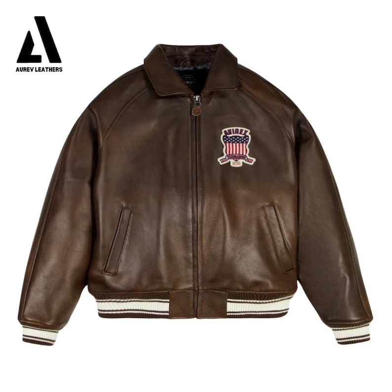 May include: A brown leather bomber jacket with a zip-up front, a collar, and a patch on the chest. The jacket has white and brown striped cuffs and hem. The brand "AUREV LEATHERS" is in the top left corner.