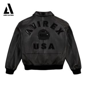 Puede incluir: Chaqueta de cuero negra con el texto "AVIREX USA" en la espalda. La chaqueta tiene cuello, pu&ntilde;os y dobladillo de canal&eacute;. El logotipo de Aurev Leathers est&aacute; en la esquina superior izquierda.